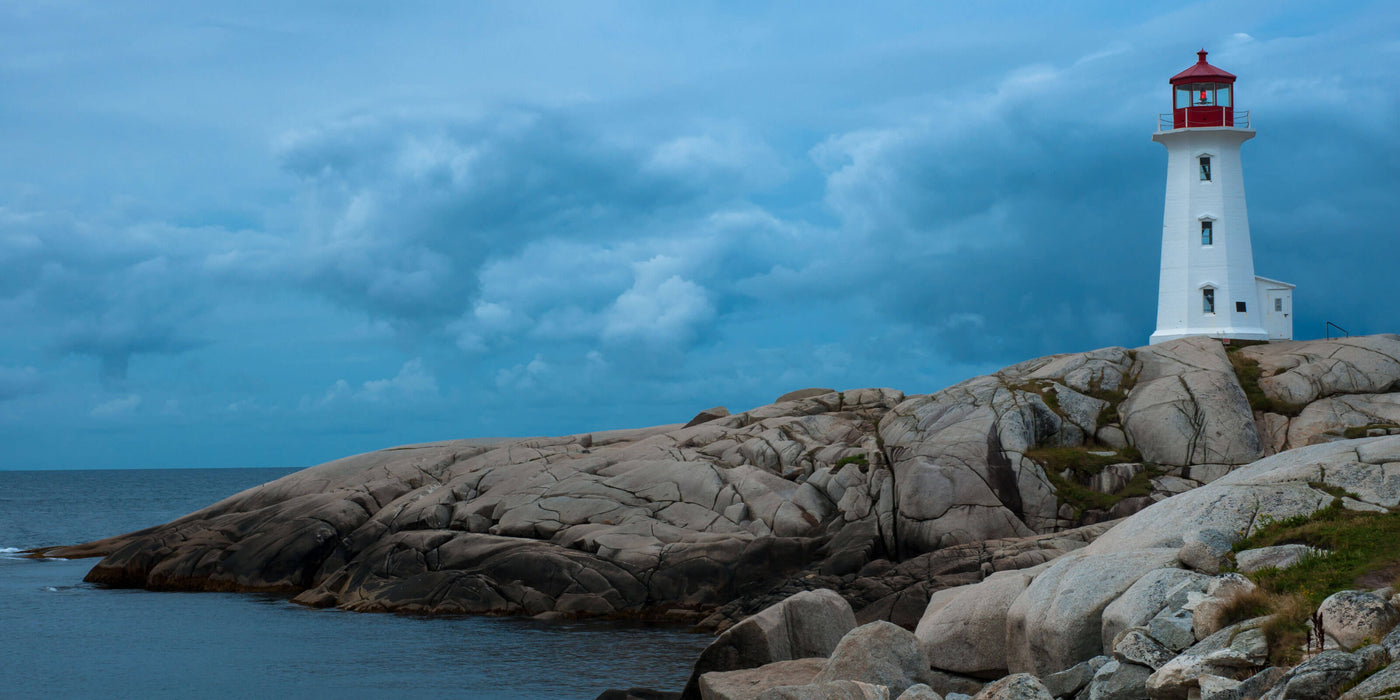 A lighthouse stands tall on a rugged shoreline, surrounded by rocky cliffs and crashing waves under a clear blue sky.