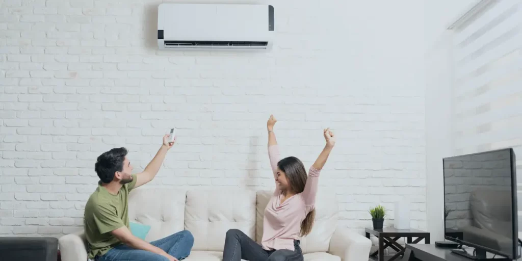 Man and woman on a sofa, arms up in excitement, turning on a new heat pump system and enjoying the comfort