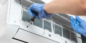 A person wearing blue gloves is using a screwdriver to fix an air conditioner
