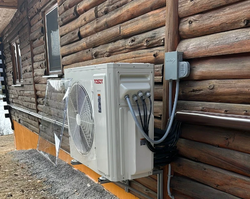 A rustic wood house equipped with a heat pump that has a wind baffle on the side, illustrating a blend of traditional architecture and modern technology.